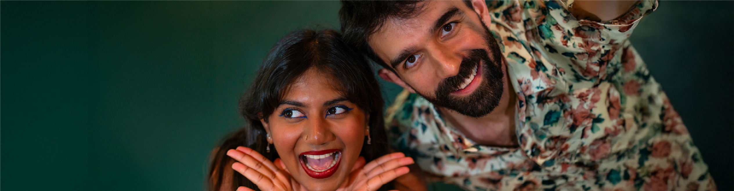 Two friends caught in a re:you kind of moment — playful, loud, and unapologetically weird. She’s mid-laugh with graphic liner and bold red lips, he's beaming in a floral shirt. Feels like the kind of joy that doesn't care who's watching.