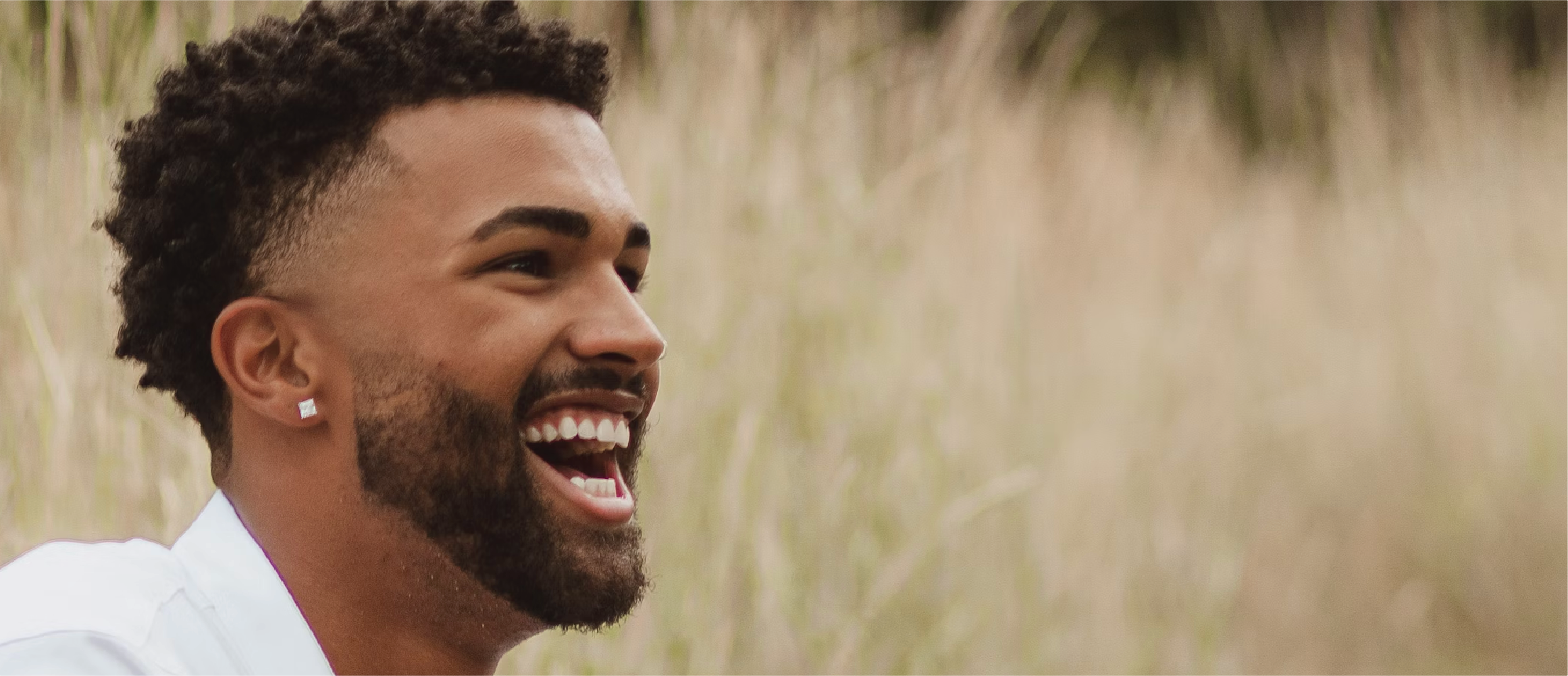 A close-up of a man laughing freely in a field, sunlight brushing his face — a re:you moment of joy without pretense.