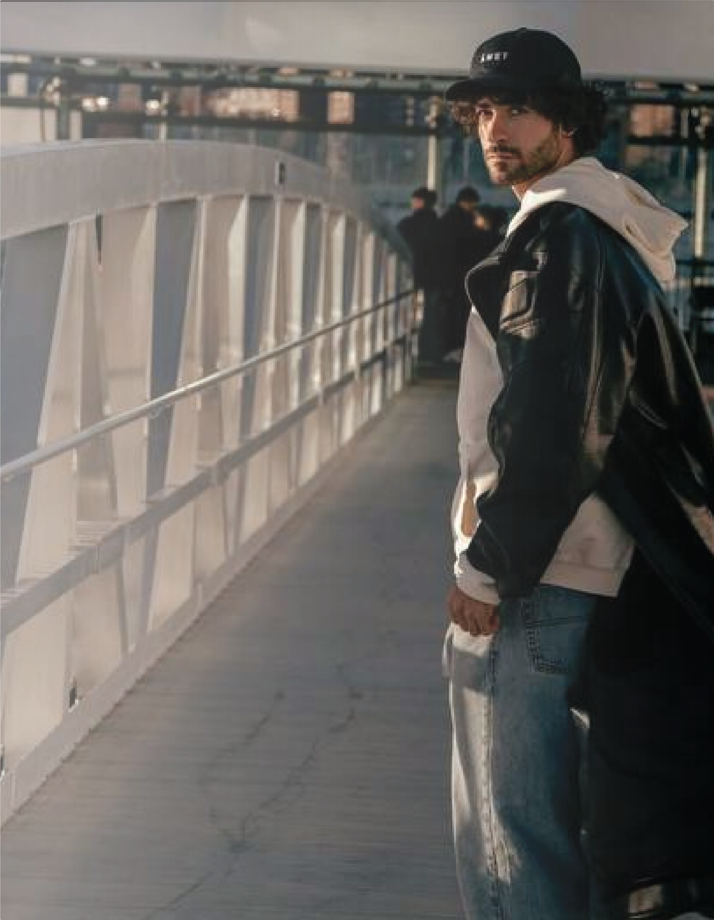 A man turns back on a pedestrian bridge in the city, caught mid-movement — a re:you moment of reflection and subtle defiance.