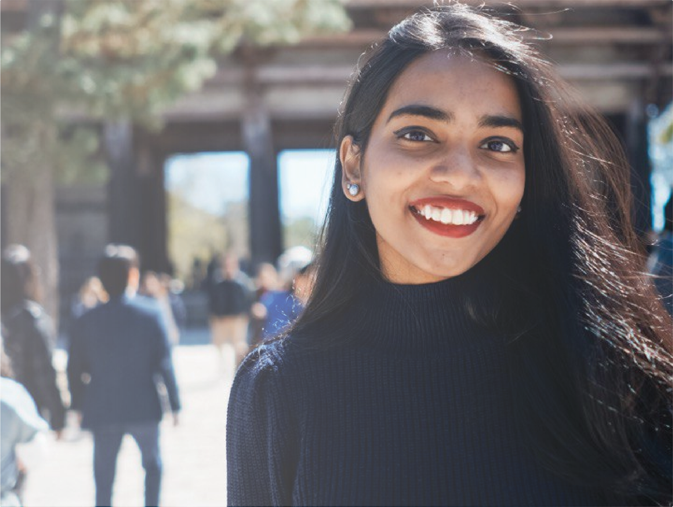A woman with bright eyes and bold lipstick smiles into the camera in a sunlit crowd — a re:you moment of feeling seen and full of life.